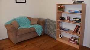 A living room with a brown sofa, a teal blanket, a bookshelf with books and games, and a framed picture on the wall.