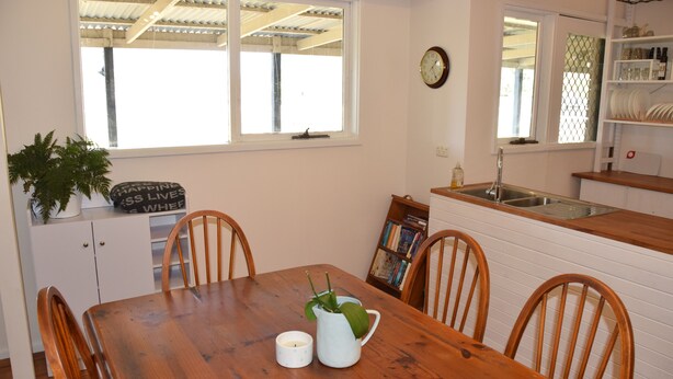 A dining area with a wooden table, chairs, a potted plant, and a bookshelf.