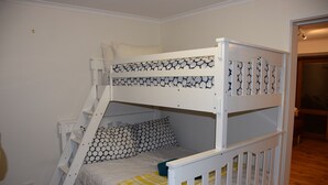 A bunk bed with patterned bedding, a ladder, and a white railing.