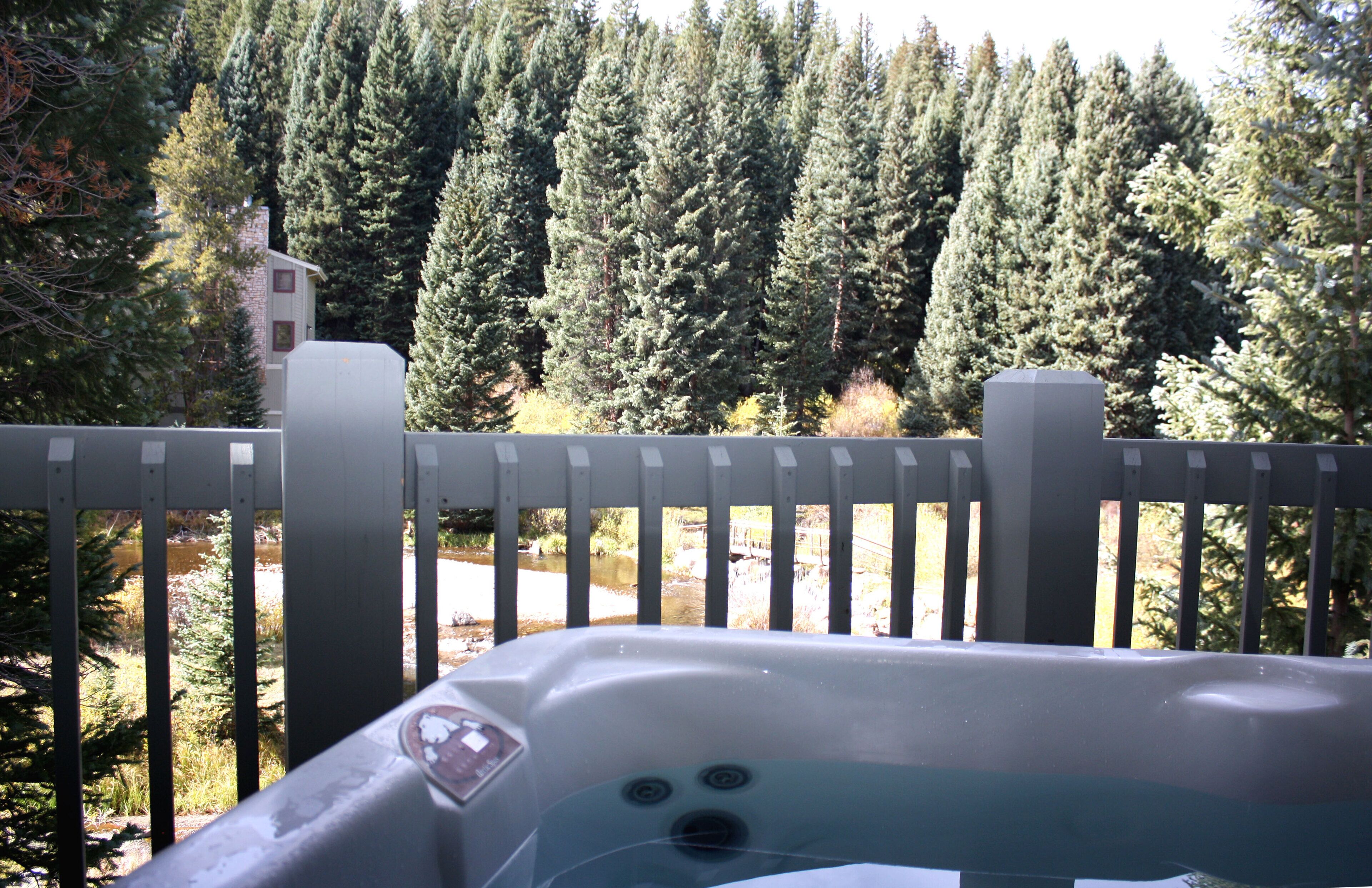 A hot tub with a view of a forest and a building in the background.