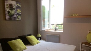 Un dormitorio con cama, almohadas, una mesita de noche, lámpara, ventana y vistas al exterior.