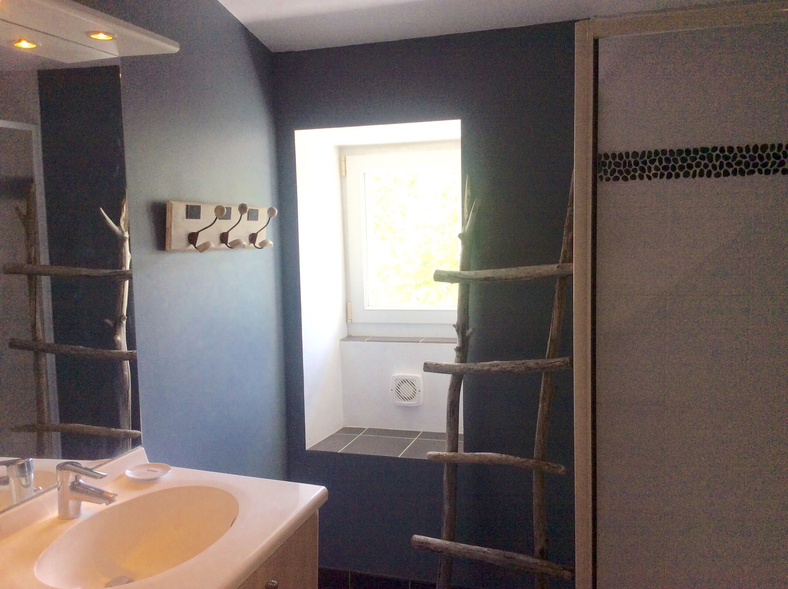 Une salle de bain avec un lavabo blanc, un miroir et une fenêtre donnant sur un paysage verdoyant.