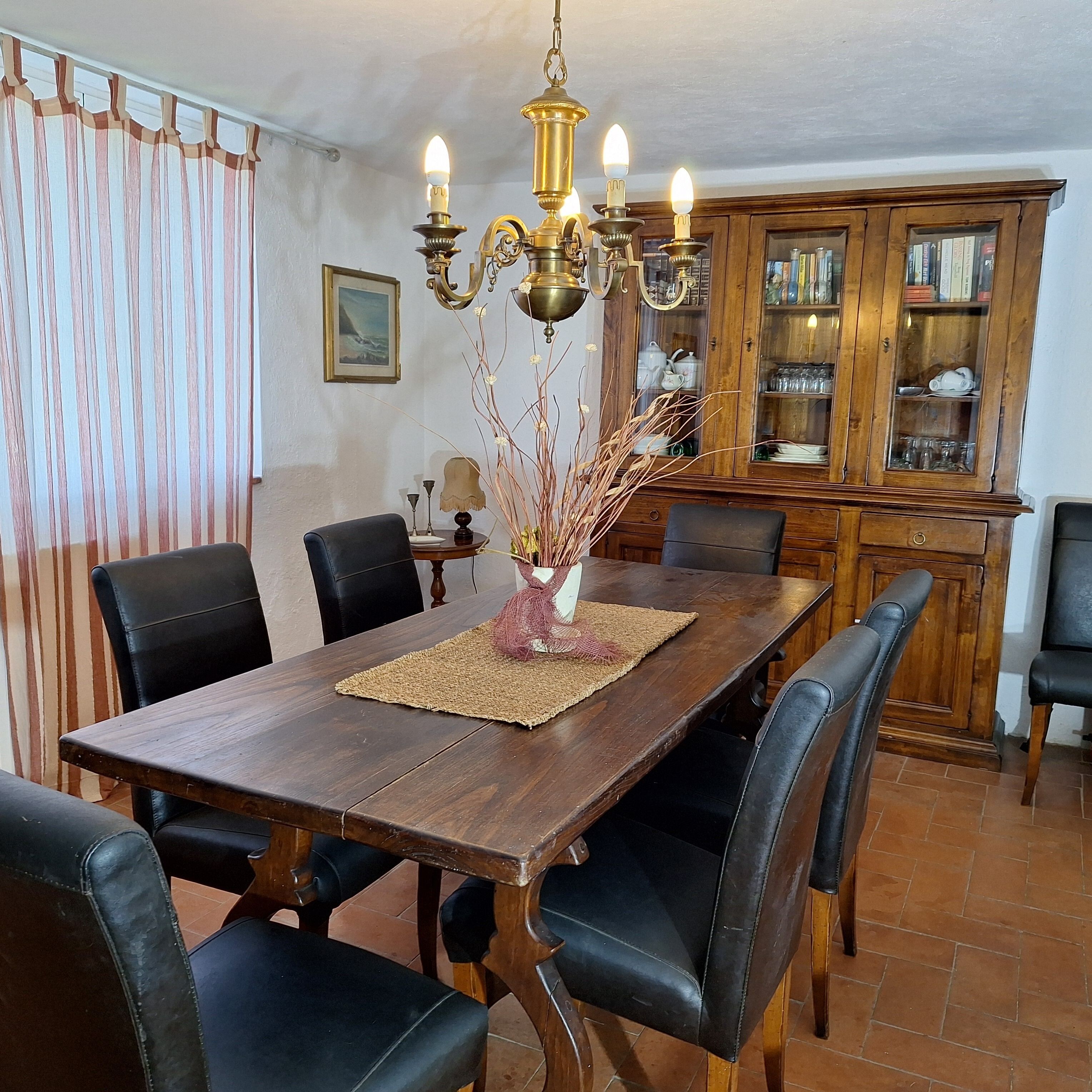 A dining area with a wooden table, black leather chairs, a chandelier, and a cabinet with glass doors.