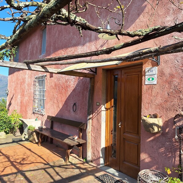 A rustic building with a wooden door, a bench, and a hanging bell.