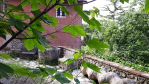 Ein rustikales Steinhaus mit Ziegeldach, umgeben von üppiger Vegetation und einer Steinmauer.
