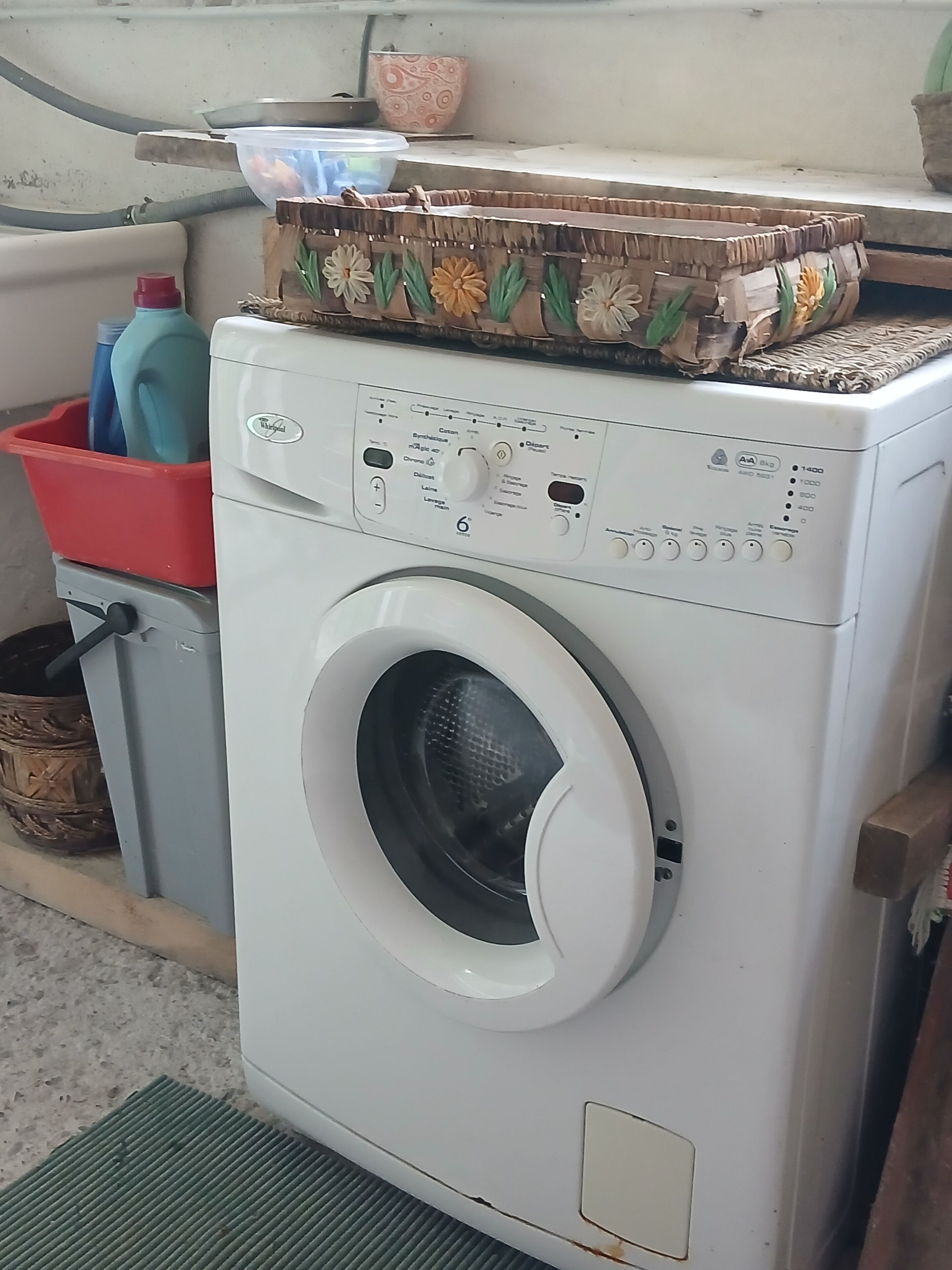 Una lavadora de carga frontal con panel de control, un contenedor de plástico rojo y una cesta tejida.