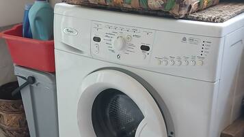 Una lavadora de carga frontal con panel de control, un contenedor de plástico rojo y una cesta tejida.
