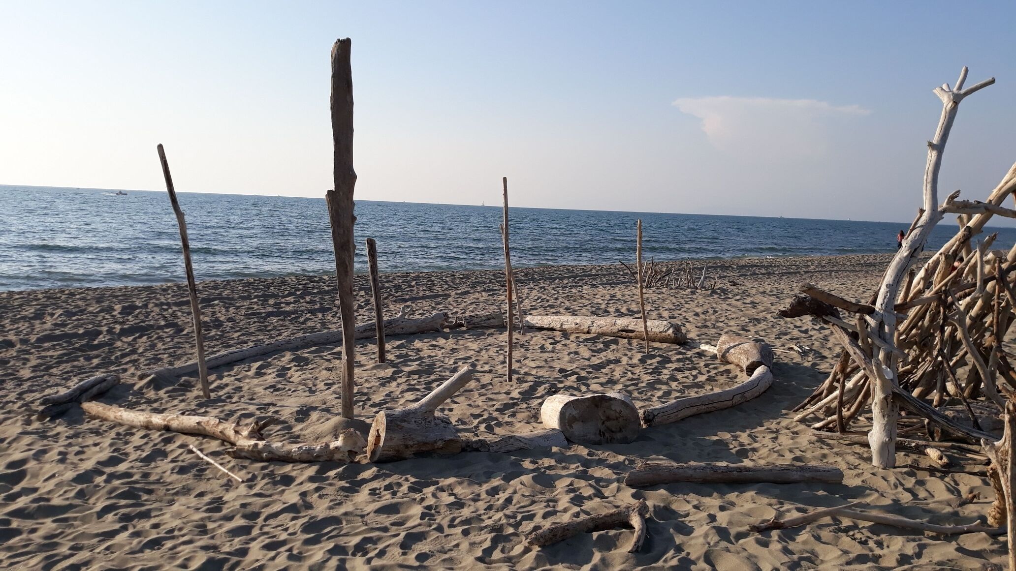 Uma praia arenosa com lenha e troncos dispostos em círculo, com vista para o mar.