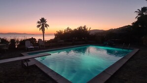 A swimming pool with lounge chairs and a palm tree, set against a sunset backdrop. - Amazing sunset from the pool, 30 meters from the sea! (Torre Delle Stelle)