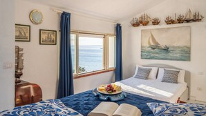 A bedroom with a bed, a window with curtains, a plate of fruit, and a sailboat painting. - Amazing sunset from the pool, 30 meters from the sea! (Torre Delle Stelle)
