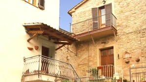 A two-story stone building with a balcony, a door, and steps leading to the entrance.