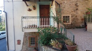 A courtyard with a stone wall, a wooden door, a balcony with a metal railing, and potted plants.