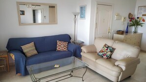 A living room with a blue sofa, beige sofa, and a glass coffee table.