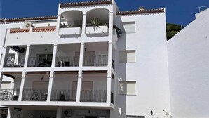 A multi-story building with balconies, a gated entrance, and a clear blue sky.