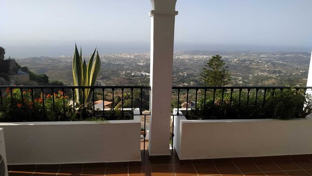 A balcony with a view of a cityscape, white walls, and a tiled floor.