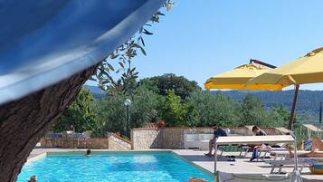 Ein Poolbereich mit Liegestühlen und Sonnenschirmen, umgeben von viel Grün und einer Steinmauer.