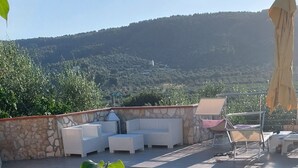 Un espace aménagé au bord de la piscine, avec une personne allongée sur un transat, un mur en pierre et une vue sur un paysage vallonné.