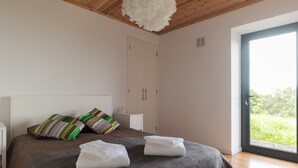 A bedroom with a bed, pillows, a nightstand, a wardrobe, and a large window. - Traditional house restored in private and quiet environment near the sea (Terra Alta)