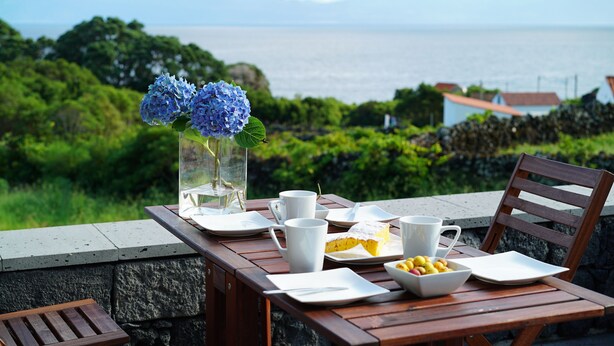 A table set with plates, cups, and a vase of flowers, overlooking a scenic view of the sea and greenery. - Traditional house restored in private and quiet environment near the sea (Terra Alta)