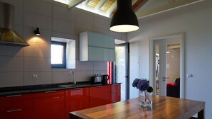A modern kitchen with red cabinets, a wooden table, and a pendant light. - Traditional house restored in private and quiet environment near the sea (Terra Alta)