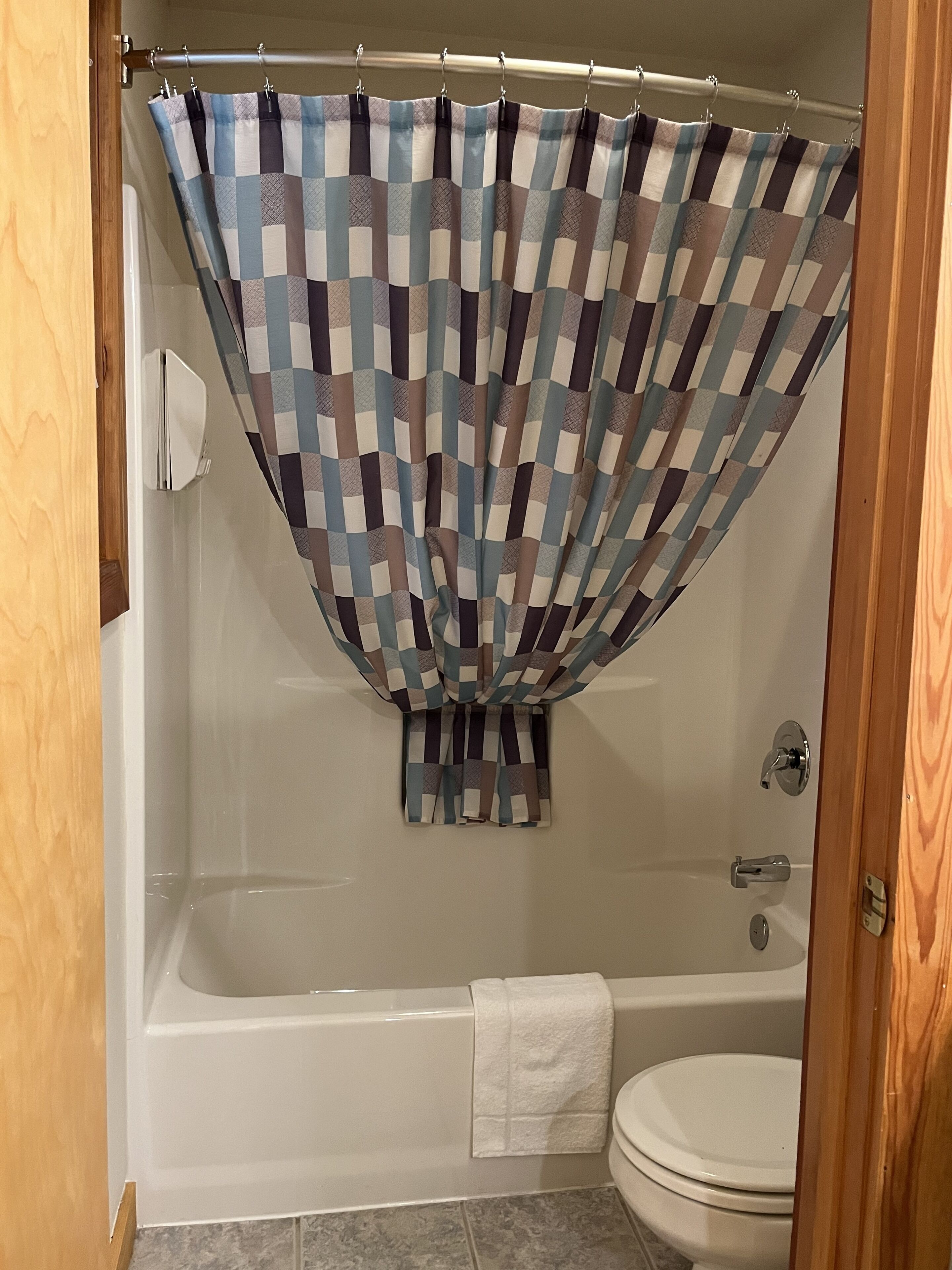 A bathroom with a checkered shower curtain, a white bathtub, and a toilet.