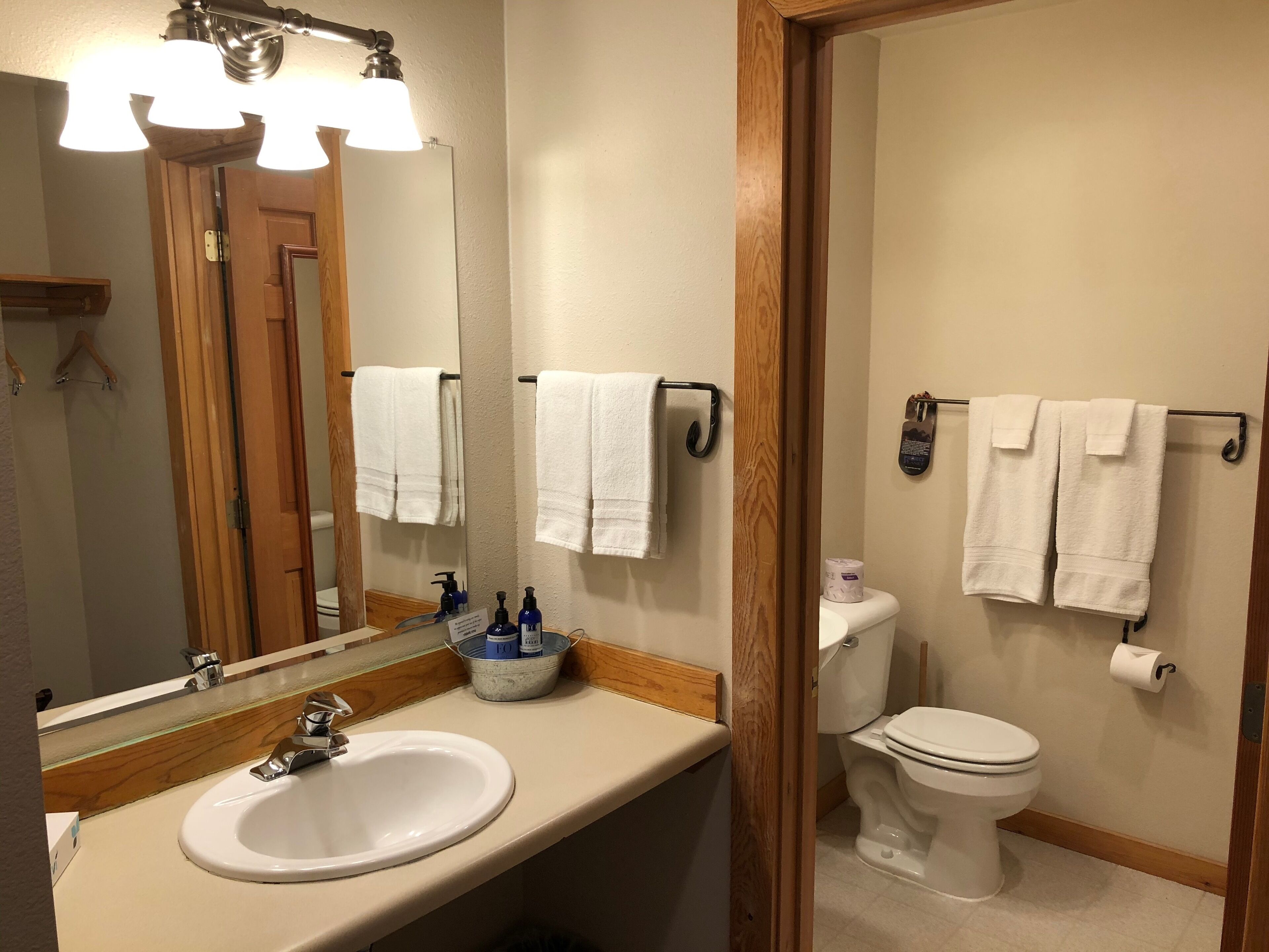 A bathroom with a white sink, mirror, and toilet. There are white towels hanging on a rack, and a sign above the sink.