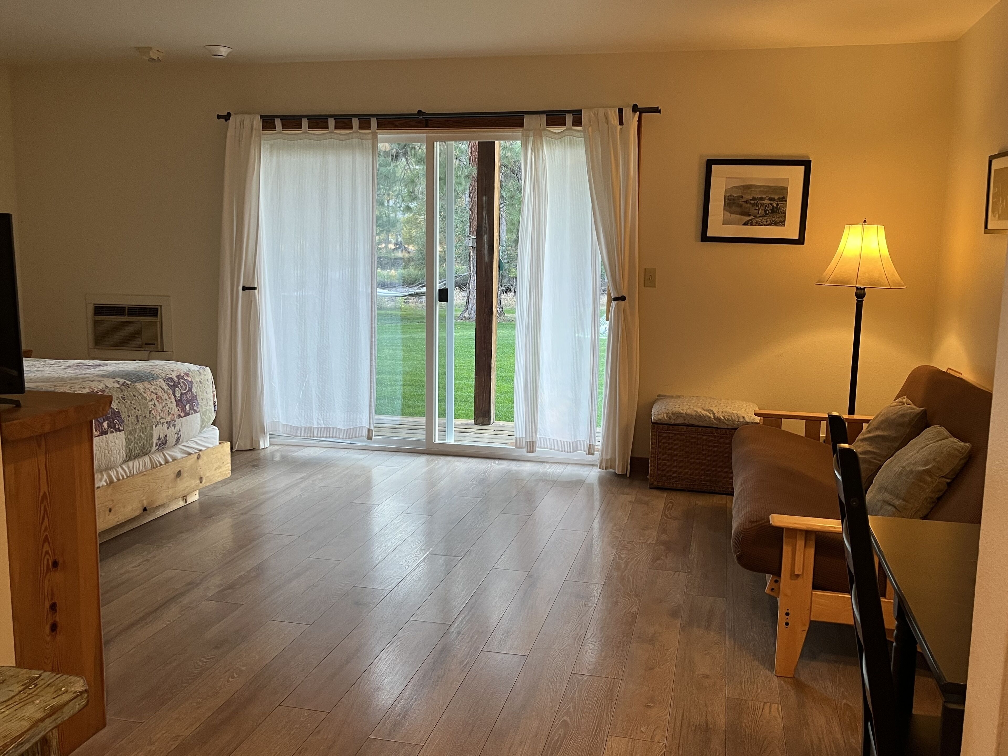 Una stanza con un letto, un divano, un tavolo in legno, una lampada e una porta scorrevole in vetro che dà su un giardino.