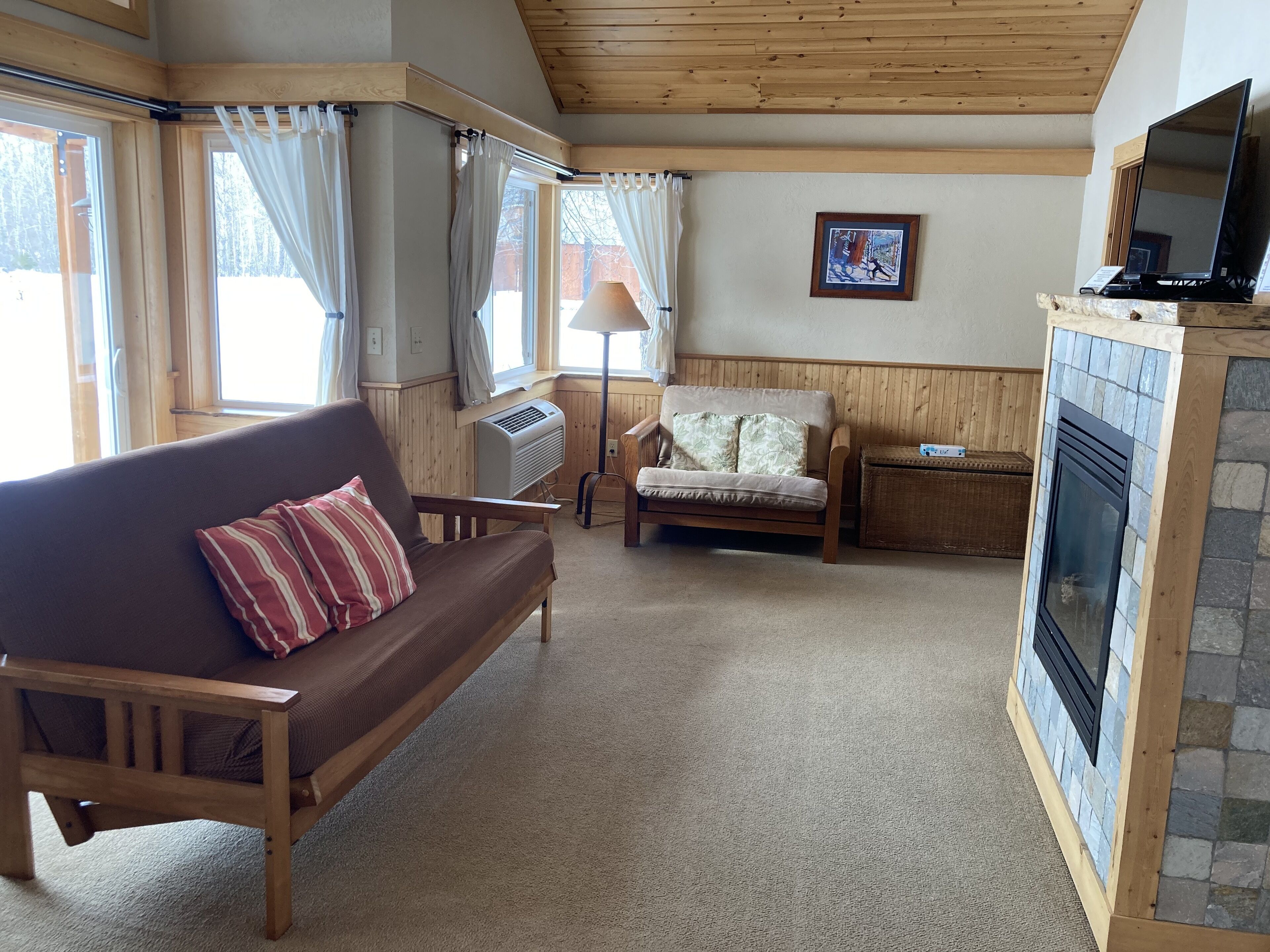 Een gezellige woonkamer met een houten plafond, een open haard, een bank, een fauteuil en een televisie.