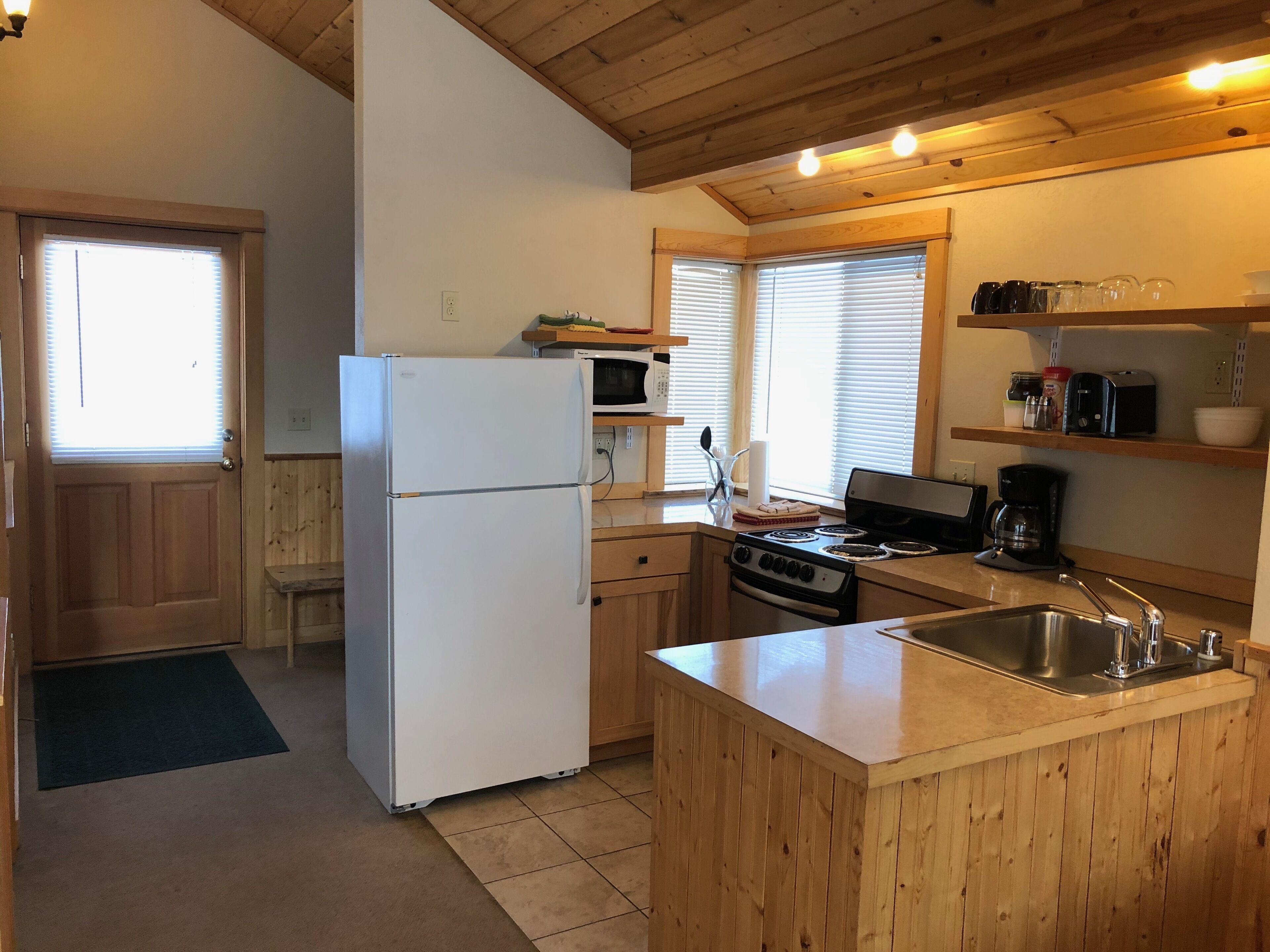 A compact kitchen with wooden cabinets, a white refrigerator, a stove, and a sink.