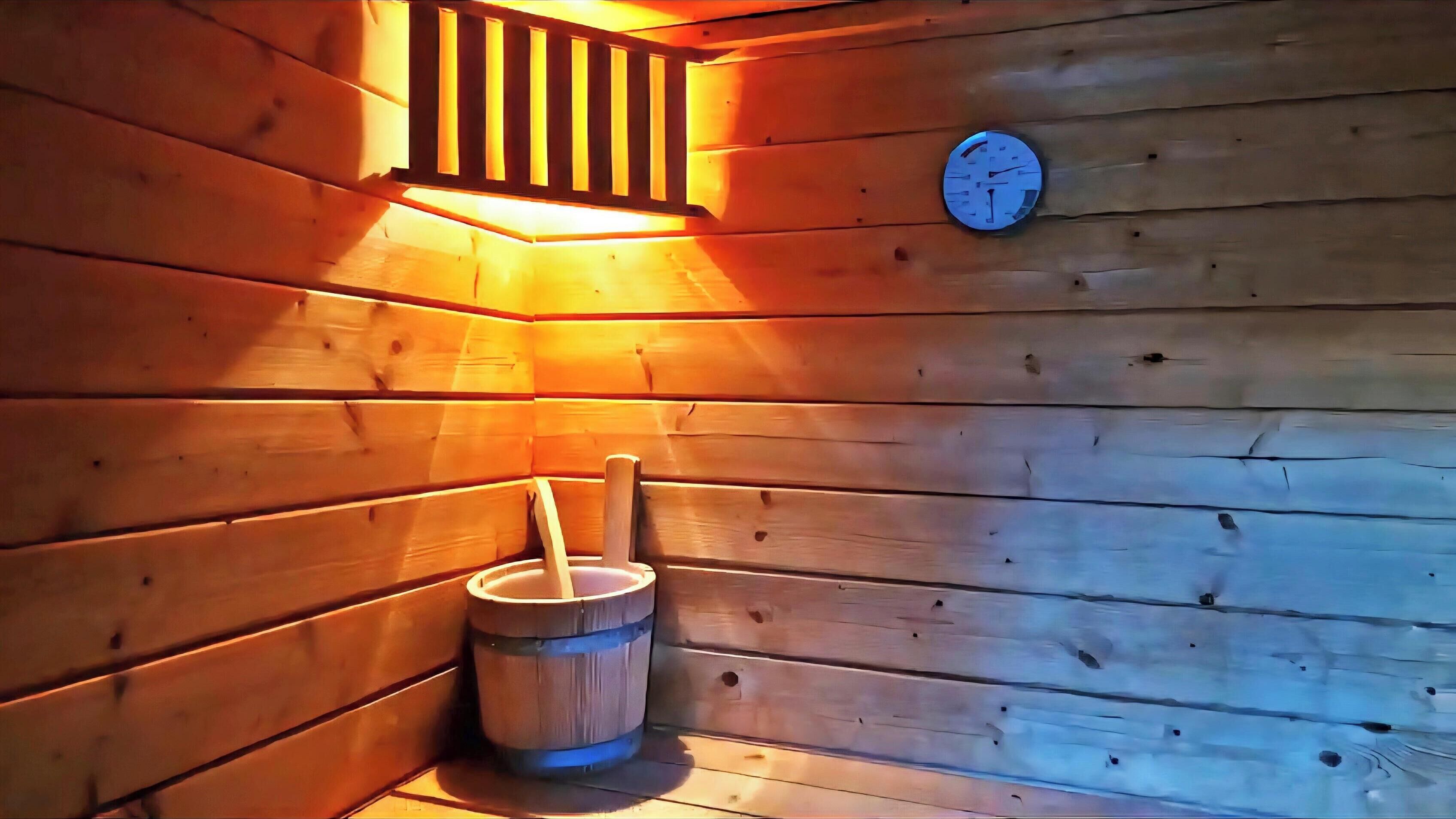 A sauna room with wooden walls, a wooden bench, a bucket, and a wall-mounted clock.