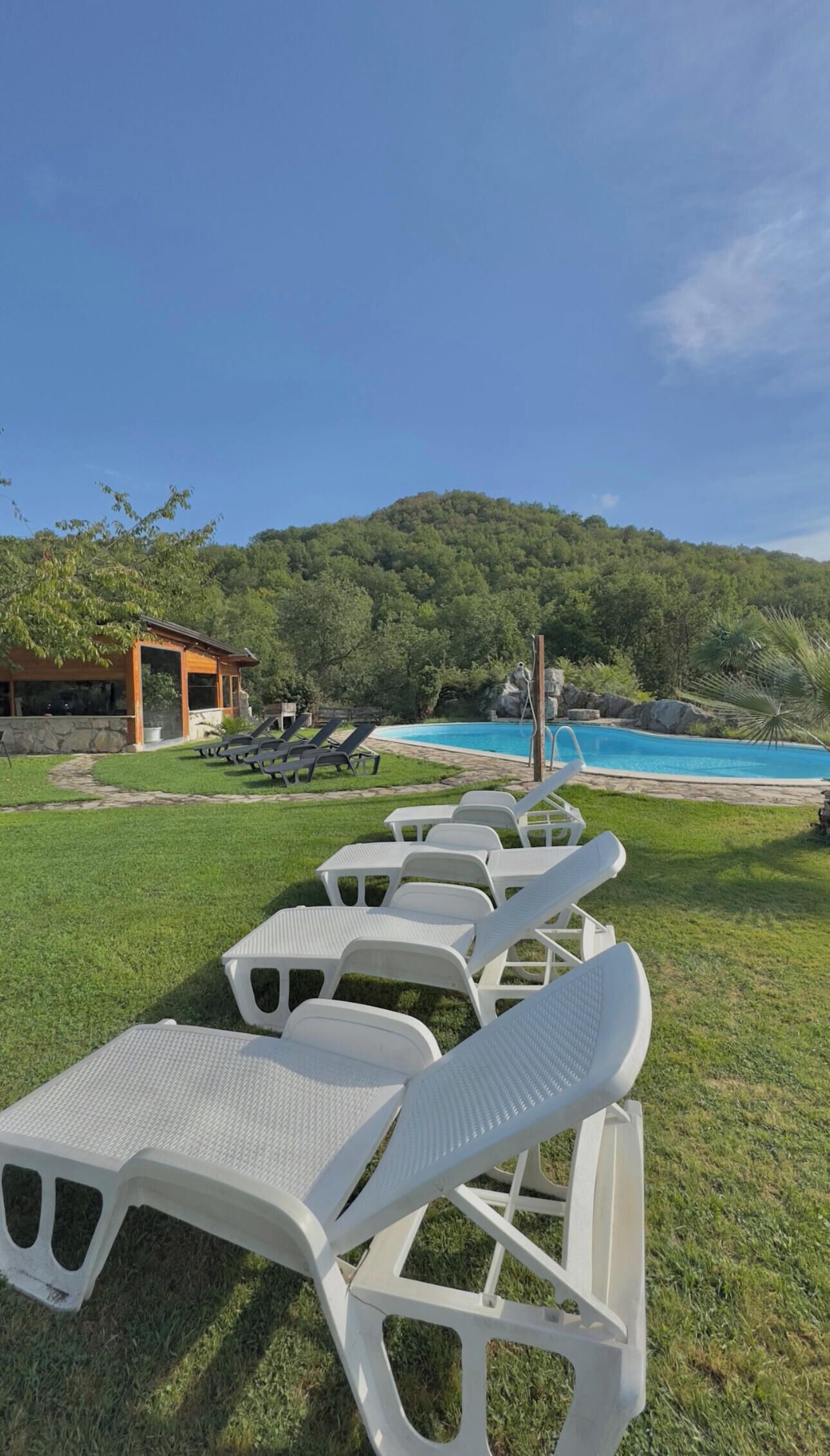 Filas de sillas de plástico blancas mirando a una piscina con una colina boscosa al fondo.