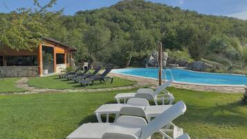 Filas de sillas de plástico blancas mirando a una piscina con una colina boscosa al fondo.
