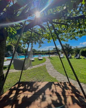 A hammock under a tree, a pool, and lounge chairs in a sunny outdoor setting.