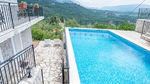 A swimming pool with a stone-tiled edge, surrounded by a stone-paved deck and a black metal railing.