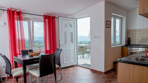 A dining area with a table and chairs, a kitchen with a stove, and a sliding glass door leading to a balcony with a view of the landscape.