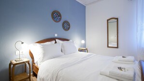 Een net opgemaakt bed met witte lakens, een bedlampje en twee decoratieve borden aan de muur.