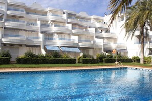 Een hotel met een zwembad, meerdere balkons en een palmboom.