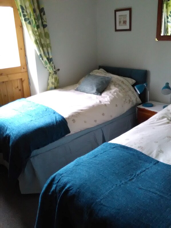 Un dormitorio con dos camas individuales, una mesita de noche con lámpara y una ventana con cortinas.