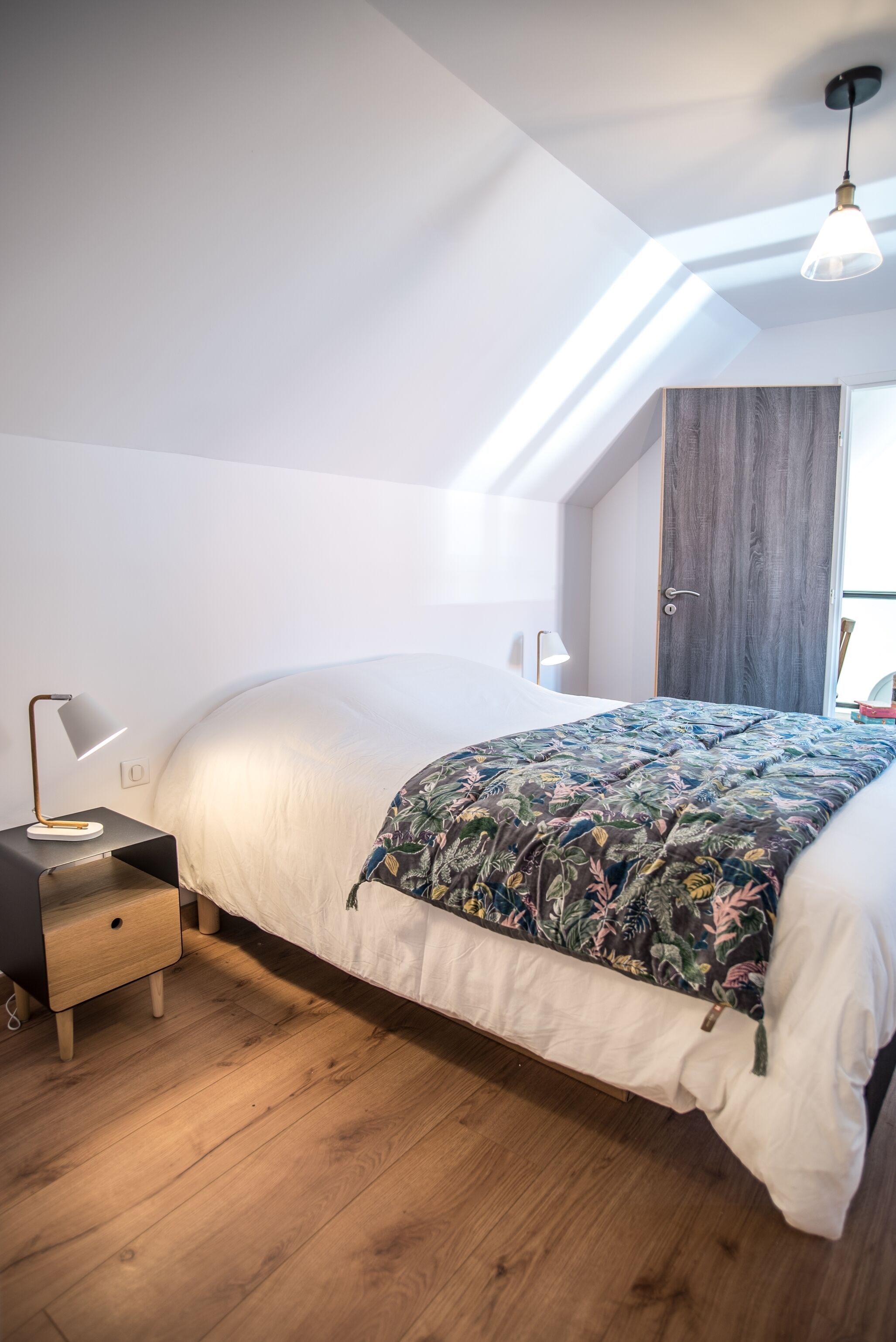 A bedroom with a bed, a nightstand, a lamp, and a wooden floor.