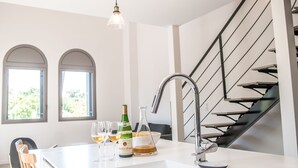 Et moderne køkken med en central ø, rustfrie hvidevarer og en trappe med gelænder i sort.