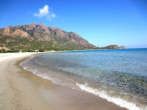 A beach with clear water, a sandy shore, and a mountain in the background. - Cozy cottage in Residence with veranda in front of the pool (Marina di Tertenia)