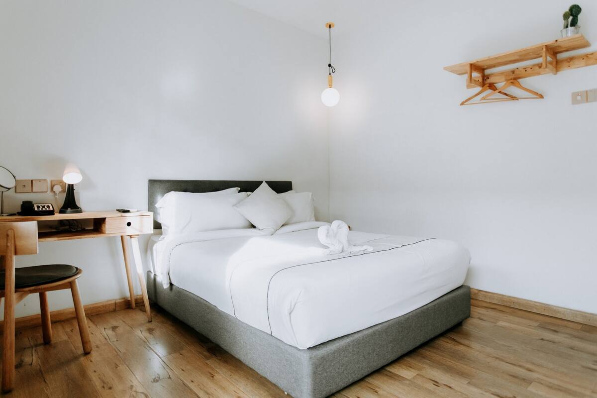 Ein ordentlich eingerichtetes Schlafzimmer mit Bett, Schreibtisch, Stuhl und einer Pendelleuchte.
