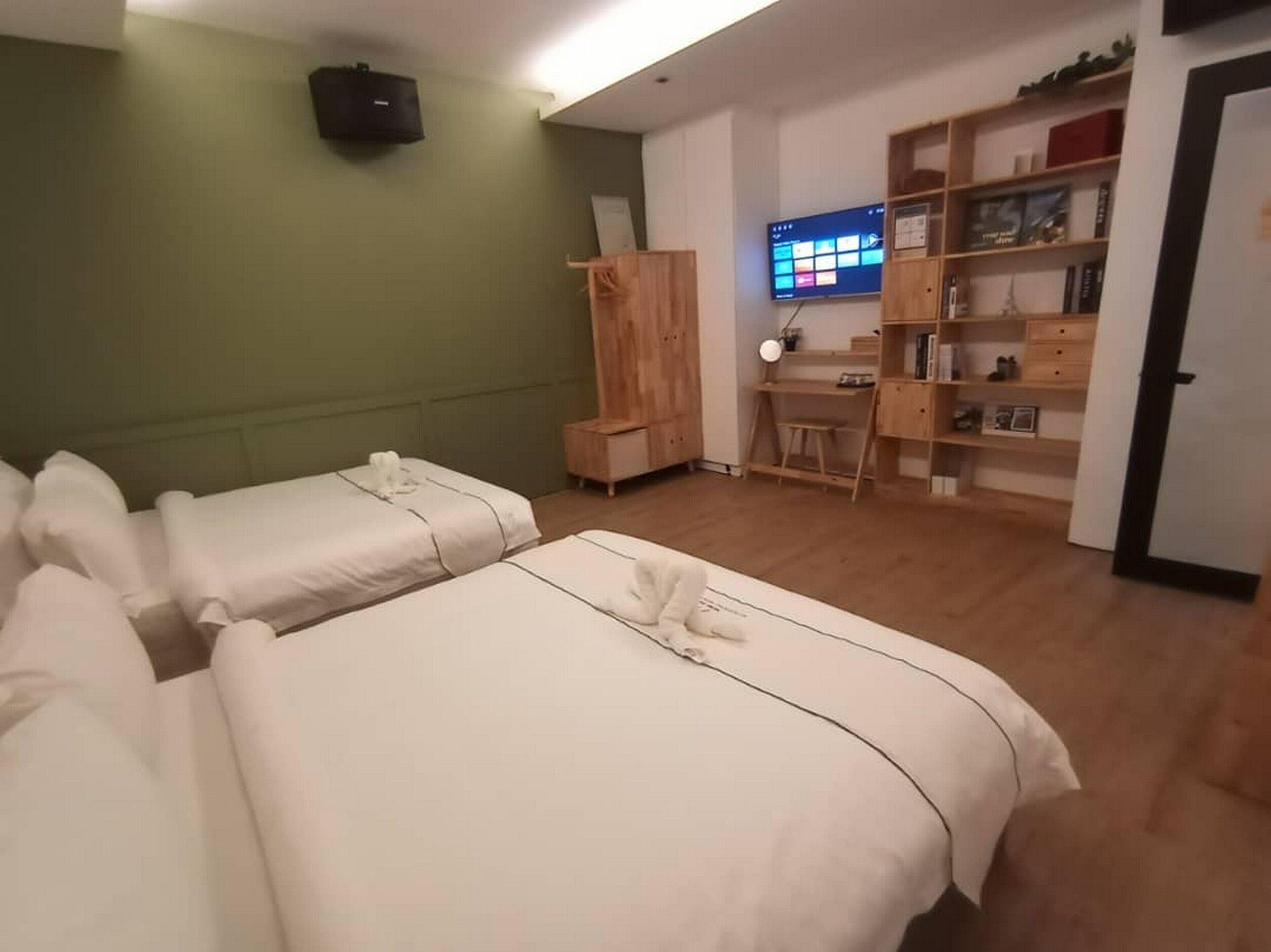 A hotel room with two beds, a desk, a TV, and a bookshelf.