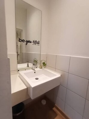 A bathroom with a white sink, a mirror, and a wall with a motivational quote.