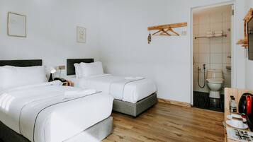 Una camera d'albergo con due letti, pavimento in legno, bagno con il water e lavandino, e un piccolo tavolino con bollitore e tazze.