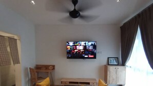 A modern living room with a flat-screen TV mounted on the wall, wooden furniture, and a ceiling fan. - MUO Resort (Muar)