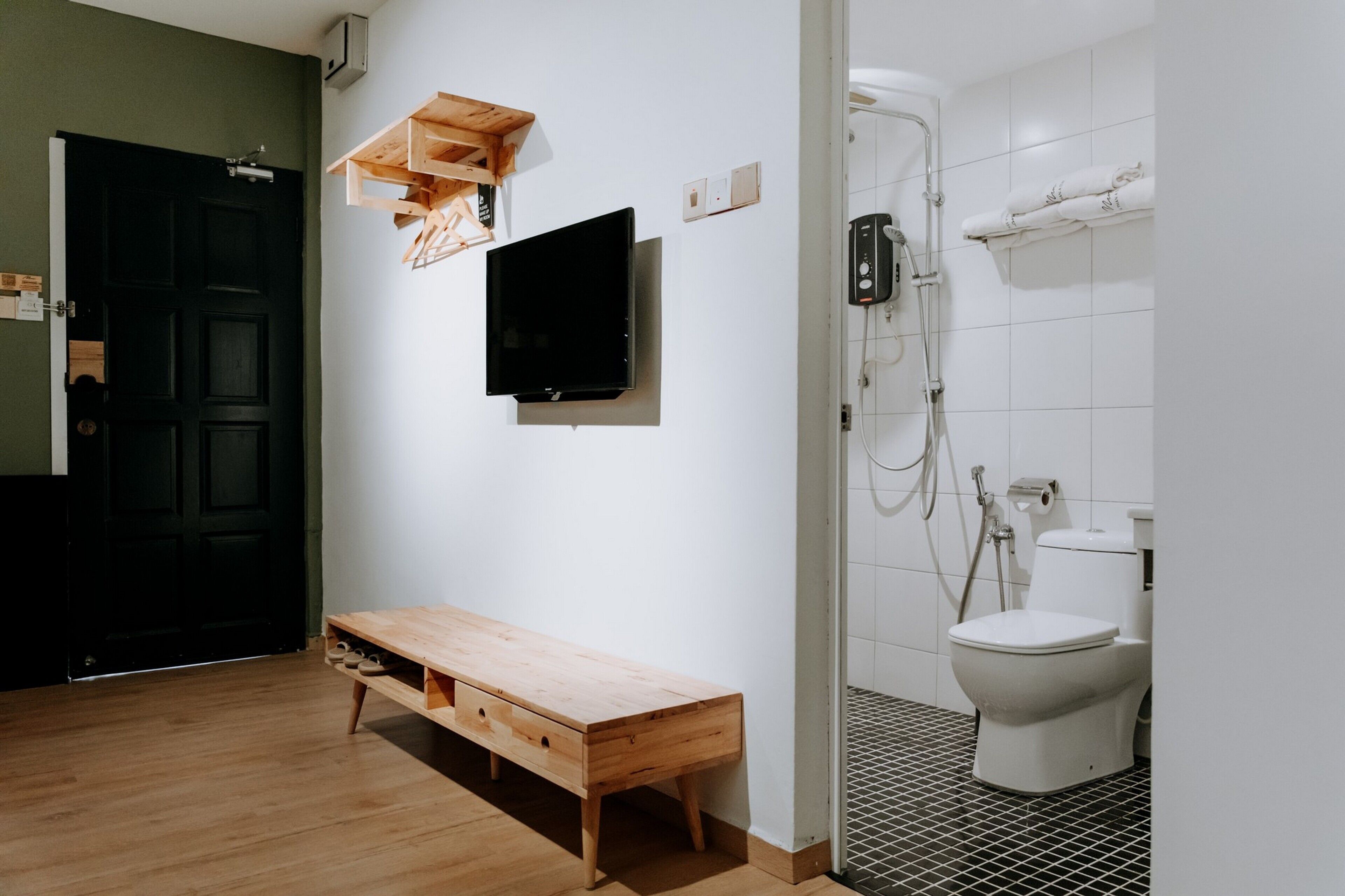 A minimalist bathroom with a wooden bench, a mounted television, and a shower area.