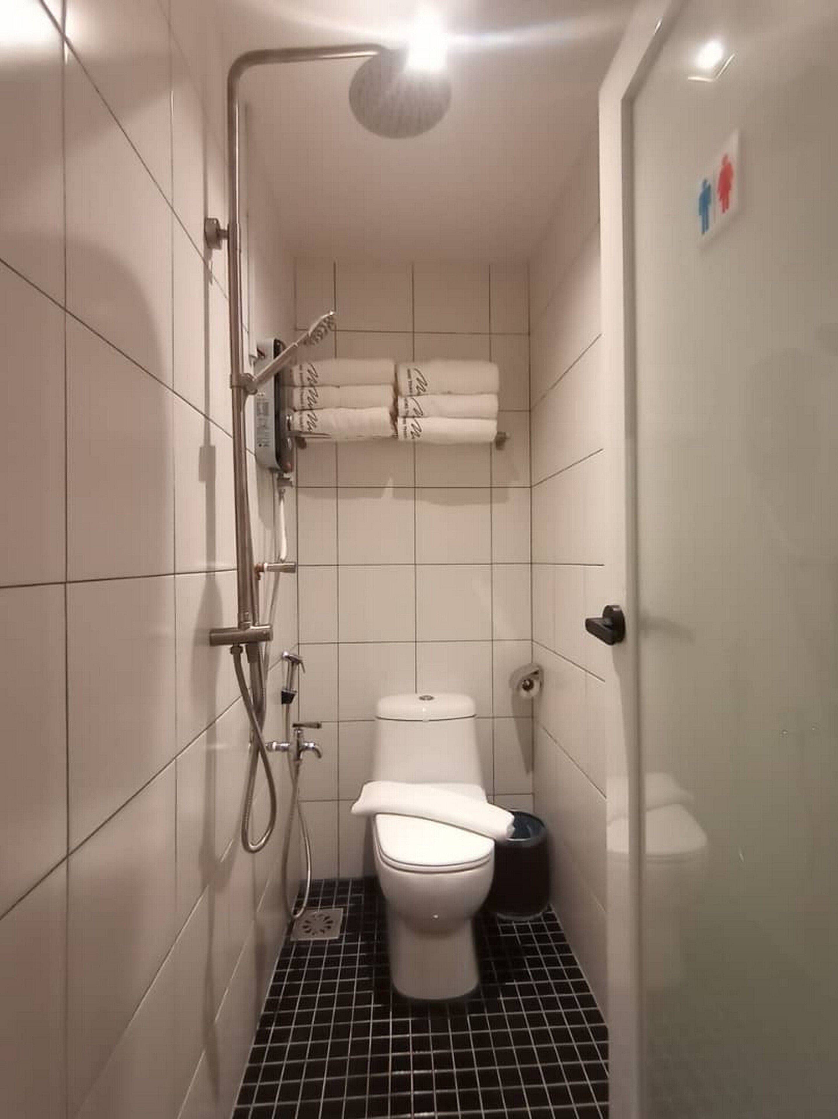 Une petite salle de bain carrelée, équipée de toilettes, d’une douche et d’un porte-serviettes.