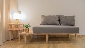 A minimalist room with a grey sofa, a small wooden side table with a lamp, and a potted plant. - MUO Resort (Muar)