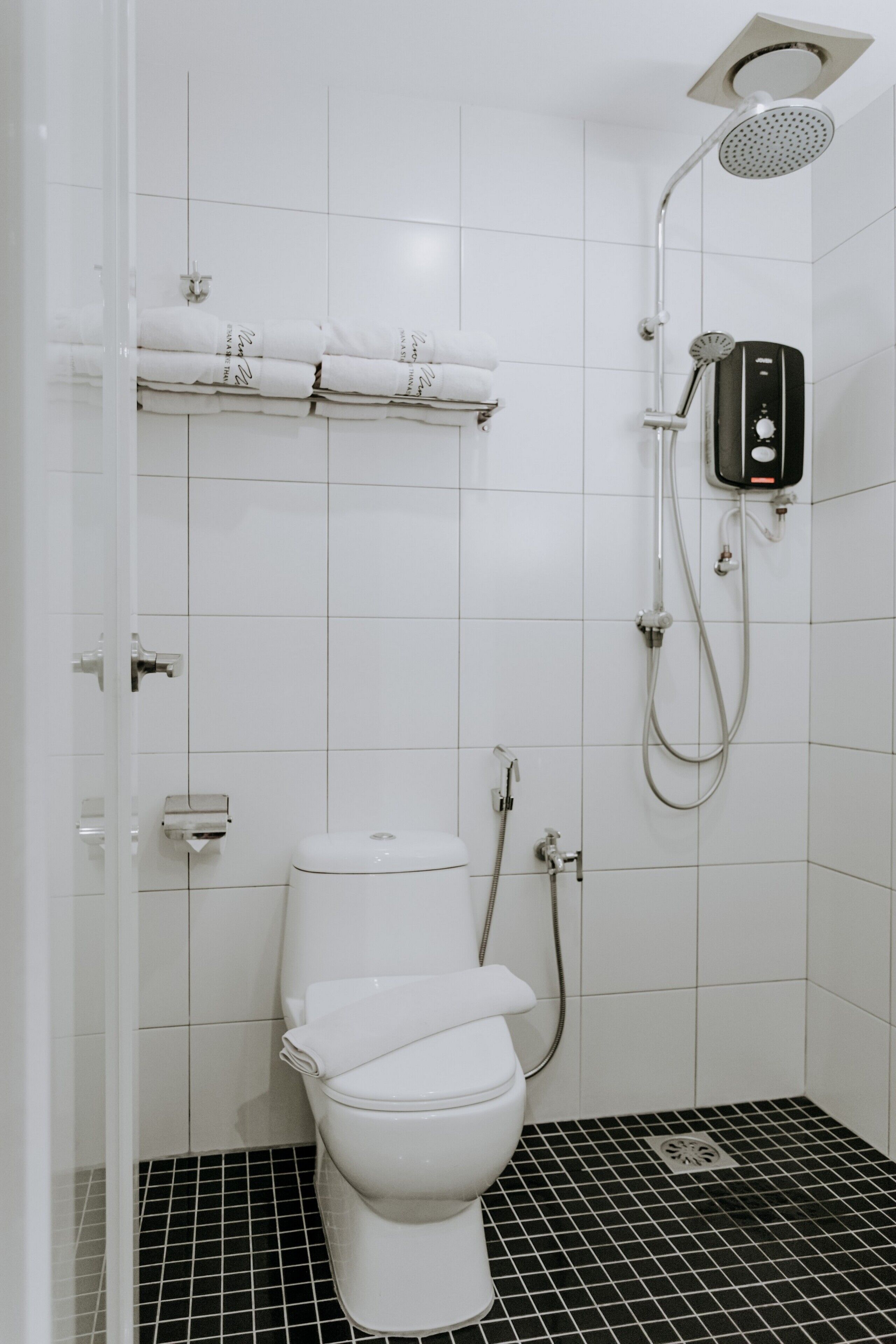 Un bagno moderno con un water bianco, una doccia con soffione a mano e un pavimento piastrellato in bianco e nero.